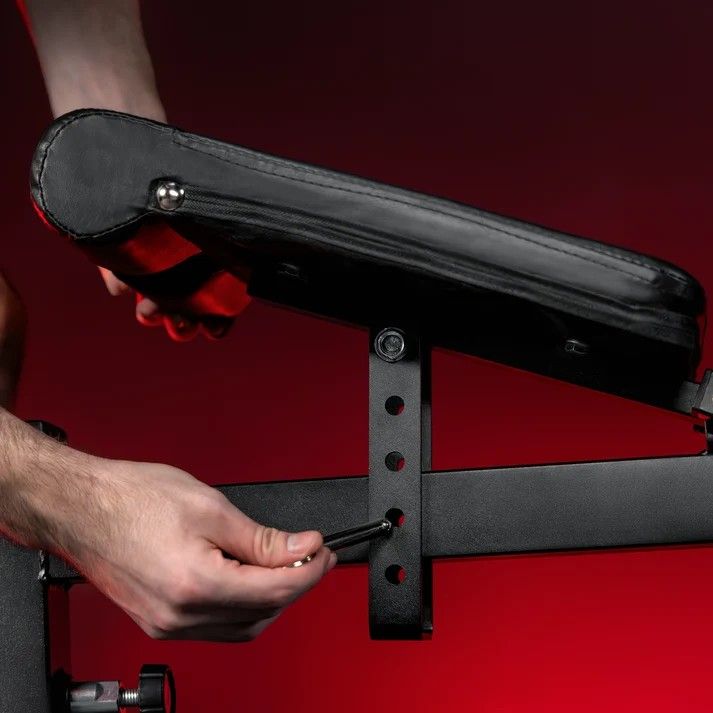 Detailní záběr na nastavování výšky opěrky posilovací lavice pomocí aretačního kolíku.