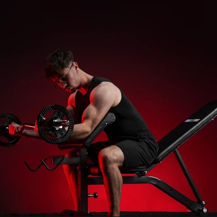 Muž provádí bicepsový zdvih s činkou na polohovací lavici s bicepsovou opěrkou v šikmé poloze